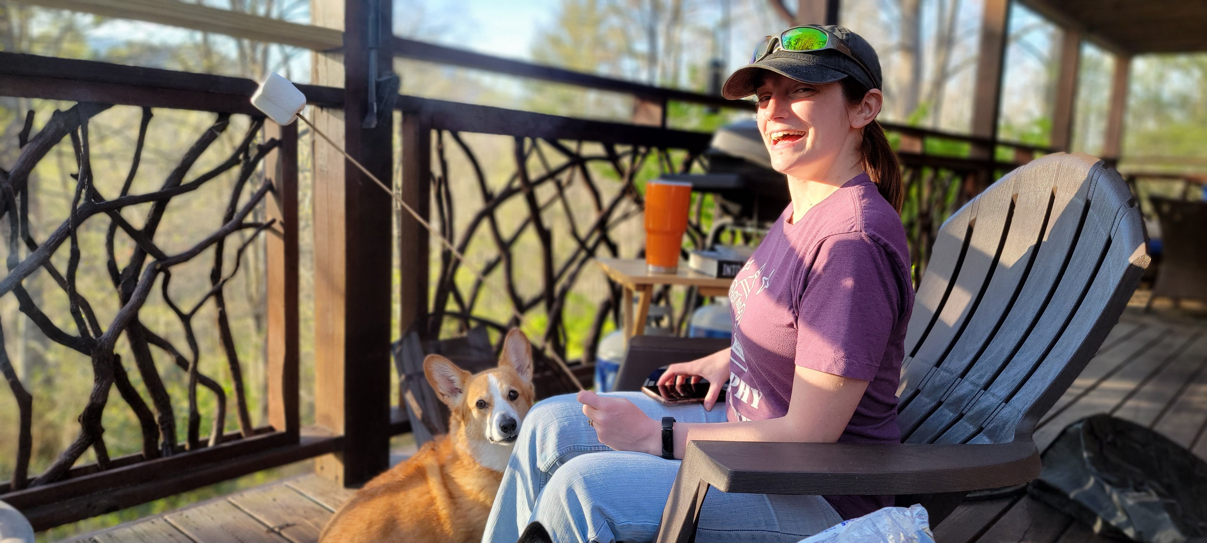 April Loebick outside holding a marshmallow on a stick. Featuring Scotch the corgi in the background