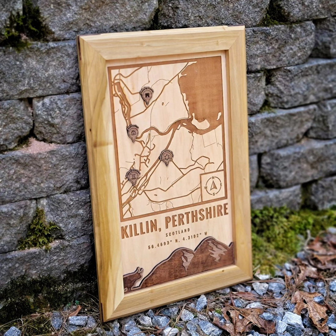 A custom wood map of Killin and Loch Tay in Scotland with four custom location icons. The accent features a silhouette of a highland cow and a mountainscape. 