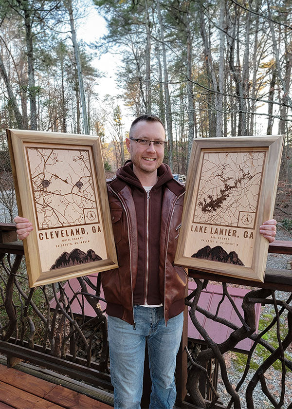 Greg Loebick, owner of G. Loebick Woodworks holding two custom location wood maps outside on a nice spring day